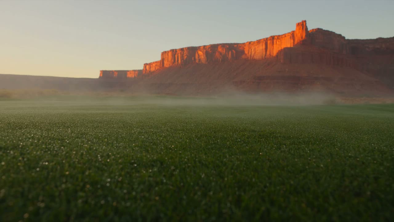 A golf fairway at sunrise below red mesa cliffs
