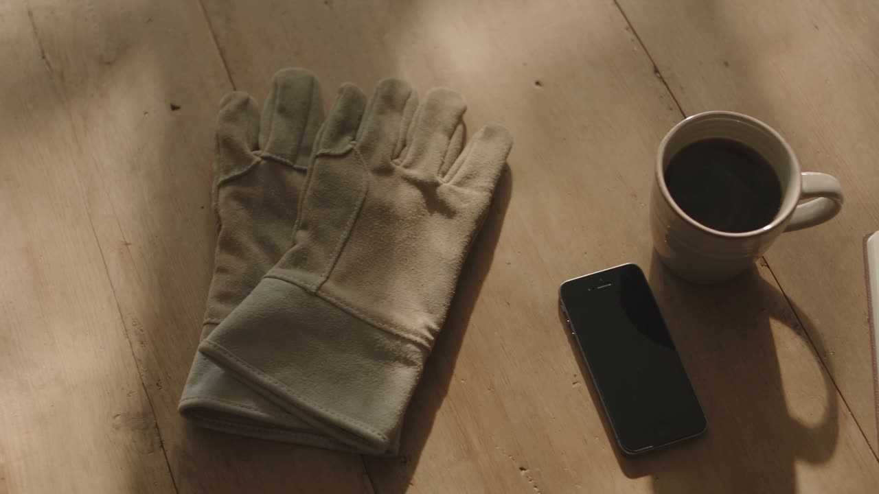 A kitchen table in morning light with a phone, a mug of coffee and a notepad